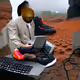 Black man in wisconsin wearing nice shoes typing words on coumputer on Mars in the rain gan 4 no sea