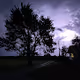 Thunderstorm and lightning behind a farmhouse and tree.