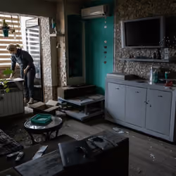 A resident cleans up smashed glass in her damaged apartment in a residential block hit by an early morning missile strike on Feb. 25, 2022, in Kyiv.
