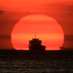 a-cargo-ship-is-silhouetted-as-the-sun-romeo-ranoco